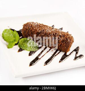 Ein Stück Kuchen mit Puderzucker bestreut und mit Minze und geschmolzener Schokolade auf einem weißen quadratischen Teller dekoriert Stockfoto