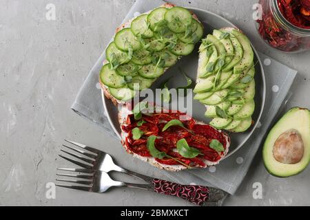 Drei Sandwiches mit Avocado, getrockneten Tomaten, Gurken, Rucola und Erbsen mikrogrün auf grauem Teller auf grauem Betongrund, Closeup Stockfoto