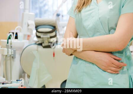 Zahnarztpraxis. Die Hände des Zahnarztes sind gefaltet und der Arzt steht in einer speziellen medizinischen blauen Uniform über dem Zahnstuhl. Ausrüstung für den Stockfoto