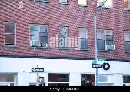 Ein Schild im Fenster mit der Aufschrift "Liebe einander" auf der Bowery in New York City. Stockfoto