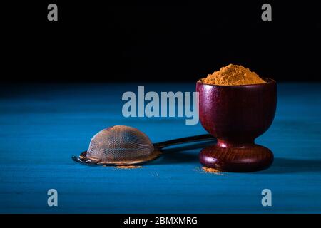 Gemahlenes Zimtpulver in Holzbecher mit Metallsieb auf blauem Holztisch mit dunklem Hintergrund. Nahaufnahme. Dieses oder ähnliche Bild war noch nicht Pub Stockfoto
