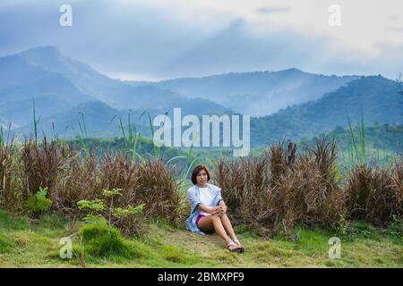 Frau und die Sonne, die durch die Wolken zu den Bäumen auf dem Berg bei Suan Phueng von Ratchaburi in Thailand scheint. Stockfoto