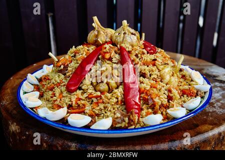 Nationalgericht Usbekisch Pilaf. Kochen in einem Kessel auf Feuer. Auf einem nationalen Teller Lyagan-Reis, von oben die Scheiben des geschnittenen Fleisches und schön verteilen Stockfoto