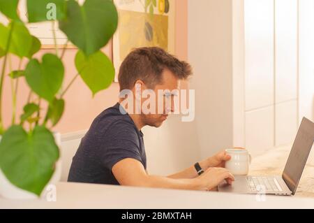 Porträt eines Mannes, der während der Sperrung des Coronavirus von zu Hause aus auf einem Laptop arbeitet. Querformat. Stockfoto