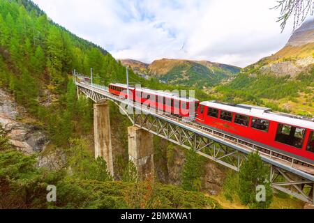 Zermatt, Schweiz - Oktober 7, 2019: Gornergrat rote Bummelzug auf der Brücke, Häuser des Dorfes und Schweizer Alpen Panorama Stockfoto