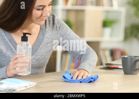 Frau desinfizieren einen Schreibtisch mit Desinfektionsmittel Gel und Tuch sitzen zu Hause Stockfoto