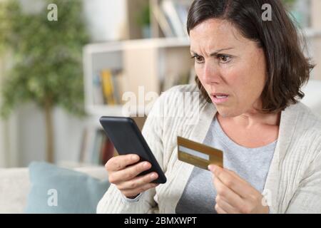 Besorgte Erwachsene Frau online zahlen auf Smartphone mit Kreditkarte sitzt auf dem Sofa zu Hause Stockfoto