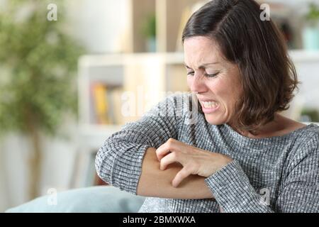 Frau mittleren Alters kratzt juckende Haut sitzt auf einer Couch zu Hause Stockfoto