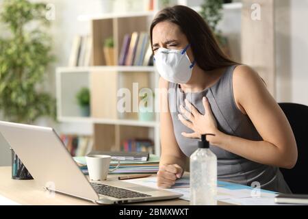 Unternehmerin mit Maske due covid-19 in Schmerzen keuchen sitzen auf einem Schreibtisch im Homeoffice Stockfoto