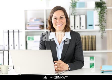 Glückliche Erwachsene Executive Frau posiert Blick auf Kamera sitzt auf einem Schreibtisch im Büro Stockfoto