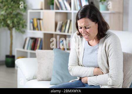 Frau mittleren Alters in Schmerzen leiden einen Bauchschmerzen hält Bauch sitzen auf dem Sofa zu Hause Stockfoto