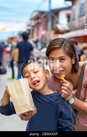 Mutter und Sohn essen Süßigkeiten auf der Straße und blurry Touristen zu Fuß Straße Chiang Khan, Loei in Thailand. Stockfoto