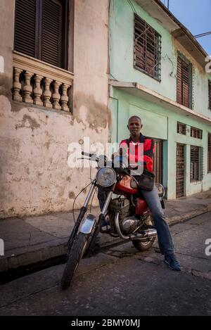 Mann, der als Motorrad-Taxifahrer arbeitet und der ein früherer Boxweltmeister war, auf seinem Fahrrad sitzt, Santiago de Cuba, Kuba Stockfoto