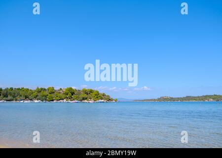 Landschaft aus türkisfarbenem Wasser mit grünen Hügel im Hintergrund und blauen Himmel während des Sommertages Stockfoto