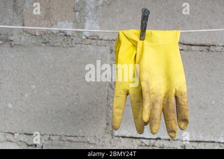 Schmutziges Gelb verwendete medizinische Gummihandschuhe am Seil mit Wäscheklammer auf Betongrund mit Copyspace Stockfoto