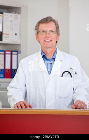 Reife lächelnde Arzt hinter dem Tresen seines Büros - Fokus auf das Gesicht Stockfoto