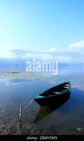 Ein einsames Holzboot schwimmt an einem nebligen Morgen auf dem Phewa See, Pokhara. Stockfoto