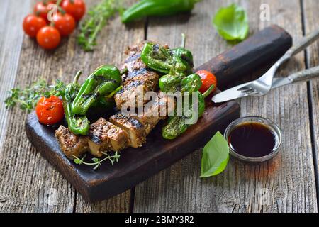 Gegrillte vegane Seitan Steaks mit Pimientos de padron und serviert mit einer Kräutersojasauce auf rustikalem Holzhintergrund Stockfoto