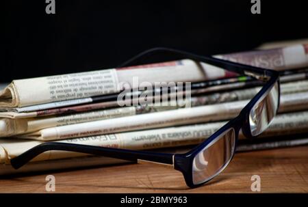 Gefaltete Stapel Zeitungen mit einem Paar blaue Lesebrille darauf. Kostenlose Informationen und Presse Konzept Stockfoto