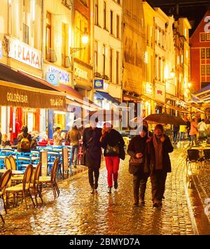 Brüssel, Belgien - 07 Oktober, 2019: Die Menschen gehen und sitzen in einem Restaurant in der Altstadt Einkaufsstraße von Brüssel im Regen in der Dämmerung Stockfoto