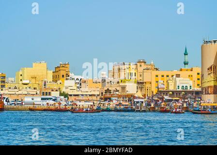 DUBAI, VAE - 2. MÄRZ 2020: Der Blick vom Dubai Creek auf den geschäftigen alten Souq Deira Abra Bootsanlegestelle mit festvertäuten Booten und alten Wohnungen, am 2. März in Dubai Stockfoto