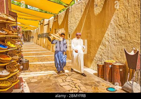 DUBAI, VAE - 2. MÄRZ 2020: Die arabischen Männer in traditioneller Kleidung gehen durch die Al Fahidi Straße, eine von ihnen trägt die große antike Skulptur, Stockfoto