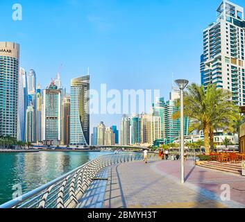 DUBAI, VAE - 2. MÄRZ 2020: Die breite Fußgängerzone der Dubai Marina mit üppigen Palmen, zahlreichen Cafés und luxuriösen Wohnhochhäusern, am 2. März in Stockfoto