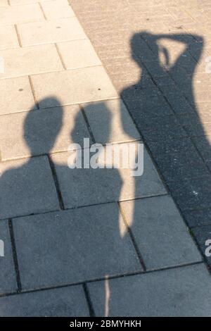 Eine Nahaufnahme des Schattens von drei Personen, die auf der Seitenpflaster auf einer Hauptstraße gehen Stockfoto