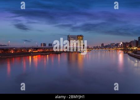 tokio, japan - märz 25 2020: Sumida-Apartments am Fluss mit Wolkenkratzern des Asahi Beer Headquarter und des Bunkyo City Hall bei Sonnenuntergang mit Kirschblüten Stockfoto