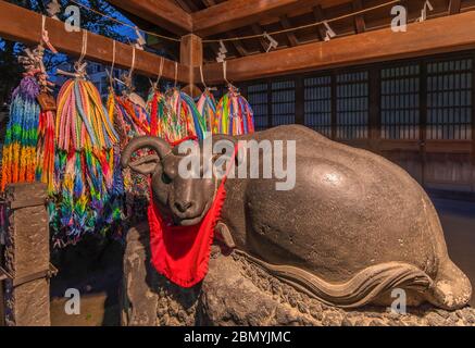 tokio, japan - märz 25 2020: Girlanden von tausend Origami-Kranichen und Steinstatue einer Nadeushi-Glückskuh mit Lätzchen, die von Gläubigen gestreichelt wurde Stockfoto