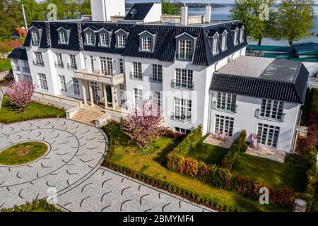 Deutschland, München, 26. April 2019: Luftaufnahme des Hofes des weißen Gebäudes bei sonnigem Wetter, Luxusleben, einem See im Hintergrund, grüner Rasen und Stockfoto