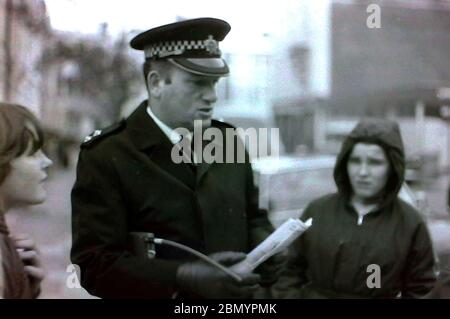 Ein leitender Polizeibeamter mit einem Radio unter dem Arm spricht in den 1970er Jahren mit jungen Leuten auf der Straße in Manchester, großbritannien Stockfoto