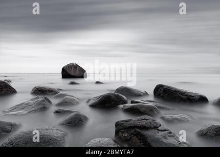 Schwarz-Weiß-Bild mit großen Steinen am Ostseestrand wurde die Bewegung von Wasser und Wolken durch Langzeitbelichtung geglättet, das Bild radi Stockfoto