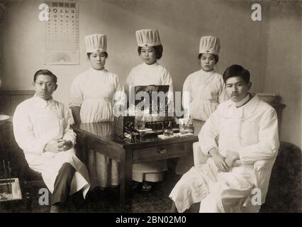 [ 1910er Japan - Japanische Ärzte und Krankenschwestern ] - Ärzte und Krankenschwestern posieren in Uniform, ca. 1910er. An der Wand hängt eine japanische Augenkarte. Silberdruck mit Gelatine aus dem 20. Jahrhundert. Stockfoto