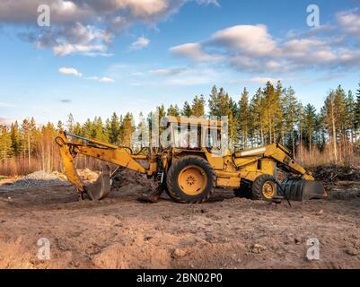 Nahaufnahme linke Seitenansicht auf alten gelben Bagger, der neben der Garage für Waldgräben steht, Vorbereitung Platz für neue Gebäude. Nordschweden, Umea. Stockfoto