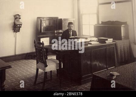 [ 1900er Japan - Western-Style Office ] - Japanischer Mann in Westernanzug bei der Arbeit in einem Western-Style-Büro mit Schreibtisch, Stühlen und Telefon, ca. 1900er. Silberdruck mit Gelatine aus dem 20. Jahrhundert. Stockfoto