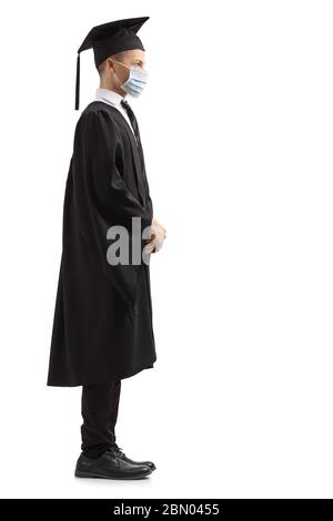 In voller Länge Profil Aufnahme eines männlichen Studenten in einem Abschlusskleid trägt eine schützende Gesichtsmaske auf weißem Hintergrund isoliert Stockfoto