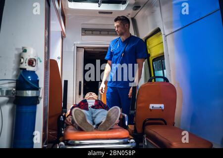 Bewusstlose Frau, die auf einer Bahre in einem Krankenwagen liegt, ein Sanitäter, der ihre erste Hilfe leistet Stockfoto