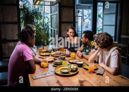 Fünf junge Freunde sitzen am Tisch in einem Café, plaudern, hav Stockfoto