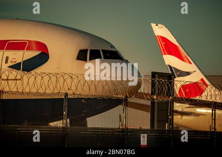 Die Nase eines Flugzeugs von British Airways neben dem Schwanz eines anderen hinter einem Stacheldrahtzaun und ohne Drohnenschild bei Sonnenuntergang. Stockfoto