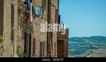 Kleidung hängt an der Seite einer alten rustikalen mittelalterlichen Hauswohnung in Montepulciano, Toskana, Italien mit Feldern und blauem Himmel im Hintergrund Stockfoto