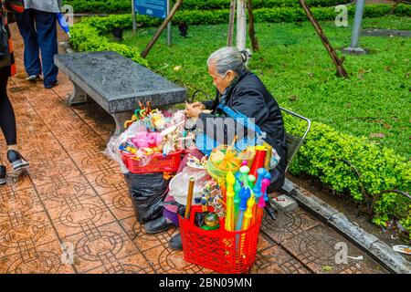 Eine alte Frau verkauft billige Plastikspielzeug in der Nähe Hoan Kiem See, Innenstadt von Hanoi, Nord-Vietnam, Südostasien Stockfoto