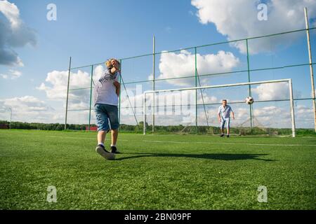 Glücklicher Vater und aufgeregt Sohn spielen zusammen Fußball auf einem grünen Fußballfeld läuft auf Gras treten den Ball in. Vater und Junge Beziehung und Stockfoto