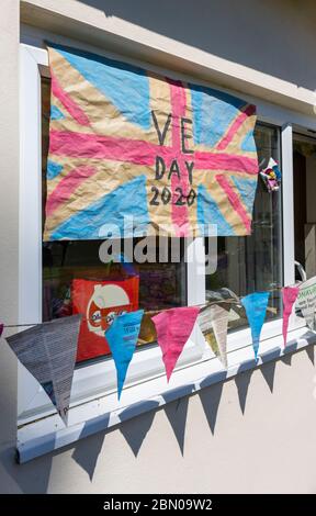 Bunte hausgemachte Union Jack Flagge und Bunting zum VE Day, 8. Mai 2020, an der Wand und Fenster eines Hauses in Surrey, Südostengland Stockfoto