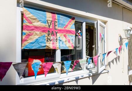 Bunte hausgemachte Union Jack Flagge und Bunting zum VE Day, 8. Mai 2020, an der Wand und Fenster eines Hauses in Surrey, Südostengland Stockfoto