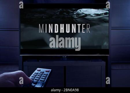 Ein Mann zeigt eine TV-Fernbedienung auf den Fernseher, der den Mindhunter Haupttitelbildschirm anzeigt (nur redaktionelle Verwendung). Stockfoto