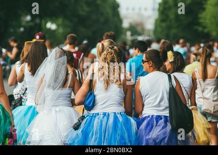 Moskau, Russland - 1. JUNI 2014: Eine glückliche Braut in einem Schleier, umgeben von Brautjungfern und einer Menschenmenge, geht durch den Park. Rückansicht Stockfoto