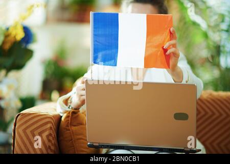 Nahaufnahme auf Frau mit Laptop versteckt hinter Französisch Flagge im Haus an sonnigen Tag. Stockfoto