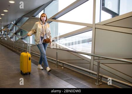 Passagierin Frau mit einer medizinischen Schutzmaske zur Verhinderung Coronavirus zu Fuß mit ihrem Gepäck in fast Flughafen / Reisestation. Reise BA Stockfoto