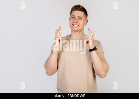 Ein schöner junger Mann drückt mit einem besorgten Ausdruck die Finger, bittet Gott, drückt die Finger mit einem erbärmlichen Blick, in der Hoffnung, dass der Chef nicht bemerkt, dass er zu spät zur Arbeit ist. Stockfoto